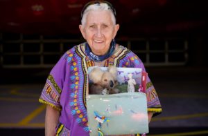 A mid-body shot of an older adult presenting their art project and smiling at the camera.