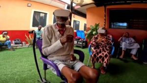 An older adult man is sitting in a chair with a VR headset on.